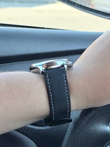 Close-up of a reviewer's wrist wearing the Lucky Fours® Shoreline watch, showing the black fabric strap with white stitching.
