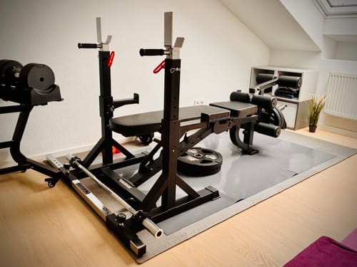 Kunde zeigt das schwarze K_SQUAT_1_Pack1/2 Rack mit einer Hantelbank in einem Heim-Fitnessstudio.