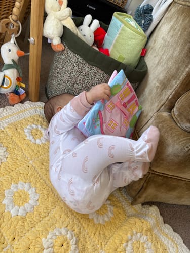 Reviewer's baby lying on a yellow blanket and playing with the colorful Montessori Soft Book.