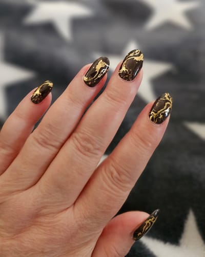 Kundin zeigt ihre langen, mandelförmigen Nägel mit dem eleganten Black Magic Marble UV-Gel-Design.