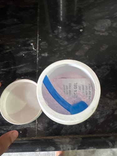 Reviewer's open tub of Wellcore Creatine Monohydrate, showing the pink powder and blue scoop inside on a counter.