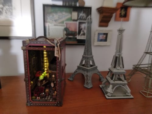 Customer's lit Eternal Midnight Paris Book Nook on a table with several small Eiffel Tower models.