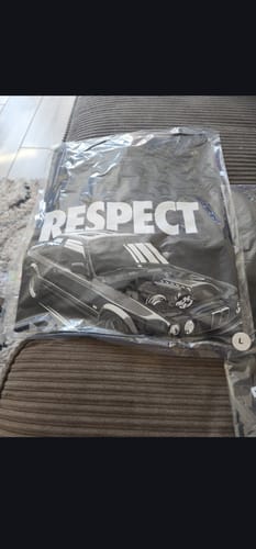 Reviewer's new black graphic T-shirt from the mystery box, shown in its packaging with a car and the word 'RESPECT'.