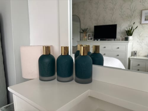 Reviewer's three dark teal Surfari bottles with gold caps arranged on a white dresser.