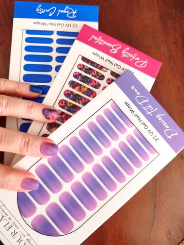 Eine Rezensentin hält die bunten „Perfectly Beautiful“ UV-Gel-Nagelfolien, während ihr Daumen das aufgetragene blumige Design zeigt.