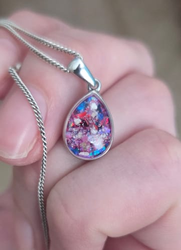 Reviewer holding their Petite Pear Drop Pendant, showing a colorful mix of magenta, pink, and blue opal with cremation ash.