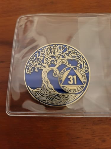 Customer's blue and gold 31-year Tree of Life sobriety medallion inside a clear protective sleeve on a wood surface.