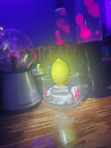 Reviewer's glowing yellow Lem Clitoral Massager displayed creatively with lava lamps and a plasma ball.