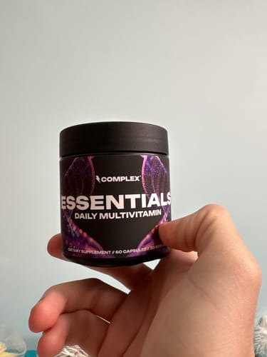 A customer's hand holding the black jar of Complex Essentials Daily Multivitamin.