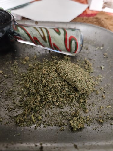 Reviewer shows the ground contents of the Single Promo Pre-Roll on a tray next to a glass pipe.