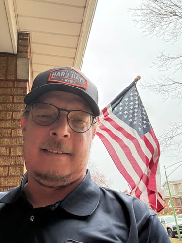 Reviewer wearing the black Hard Days Snapback Trucker hat outdoors with an American flag in the background.