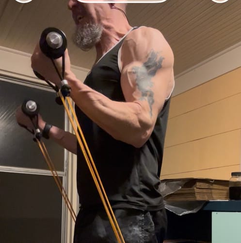 A reviewer performs a bicep curl with the Handles attached to resistance bands, showing muscle definition in their arm.