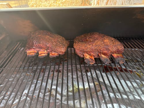 Customer's two seasoned racks of Bone-In Short Ribs cooking on a smoker grill.