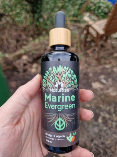 Ein Kunde hält die Flasche des Omega 3 Algenöls von Naturise mit einer Holzpipette in der Hand.