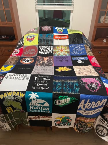 Customer's colorful Project Repat T-Shirt Quilt, made of many different shirts, spread neatly across a bed.