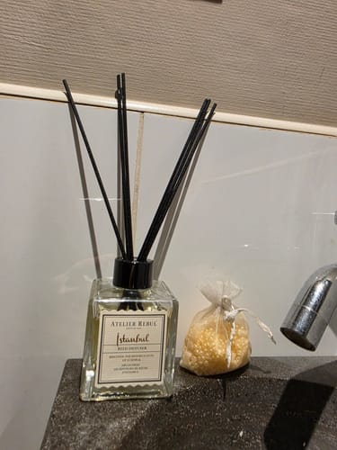Klant toont de Istanbul Geurstokjes in de glazen fles op een donker aanrecht in de badkamer.