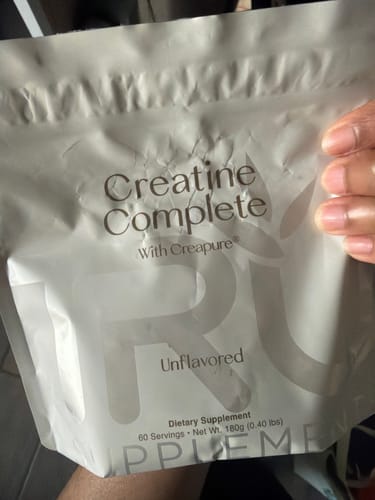 Close-up of a customer holding a white pouch of Unflavored Creatine Complete supplement.