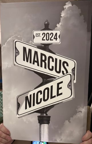 Customer holds a personalized street sign canvas with the names 'Marcus' and 'Nicole' and the date 'Est. 2024'.