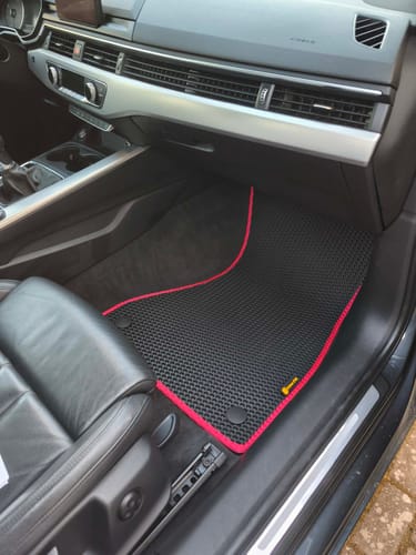 Recenzent pokazuje dopasowany czarny dywanik samochodowy z czerwoną lamówką, zamontowany po stronie pasażera.
