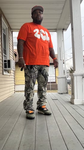 Reviewer standing on a porch wearing the Vortex Cargo Stacked Denim in black camo with a bright orange shirt.