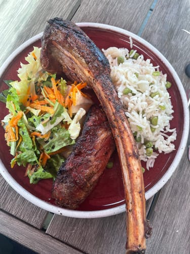 Customer's cooked USDA Choice Tomahawk Ribeye plated with rice and a fresh salad on a red plate.