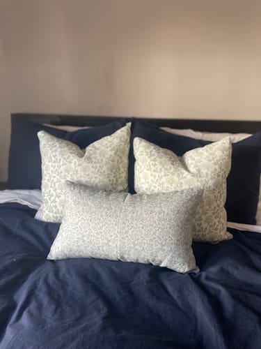 Customer's three Clem in Linen floral pillows arranged on a bed with a dark navy duvet.