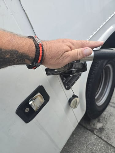 Reviewer wearing their black and orange Hard Days Paracord Bracelet on their wrist while pumping gas into a vehicle.
