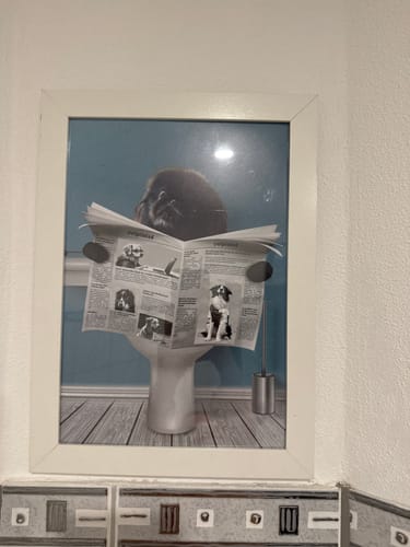 Ein Kunde zeigt das personalisierte Poster 'Wichtige Sitzung' in einem weißen Rahmen, das an einer gefliesten Wand hängt.