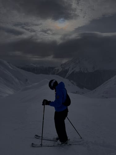 Customer in black baggy snow pants, standing on skis on a mountain.