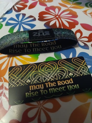 Customer's green May The Road Rise To Meet You Bracelet displayed on a floral surface with its matching card.