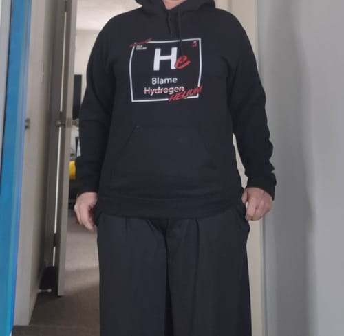 A reviewer wears the black Blame Helium unisex hoodie, showing the fit and graphic on the chest.