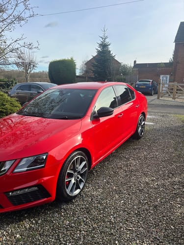 Customer's shiny red car parked on a gravel driveway, looking very clean after a wash.