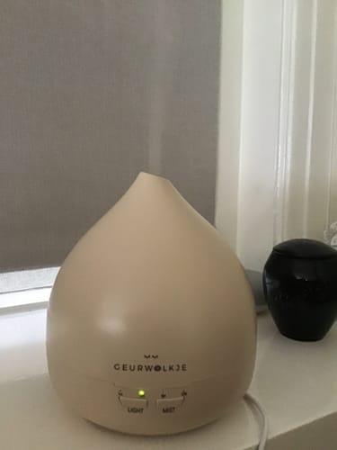 Recensent toont de nude Unity 2.0 Aroma Diffuser die aan staat op een vensterbank.