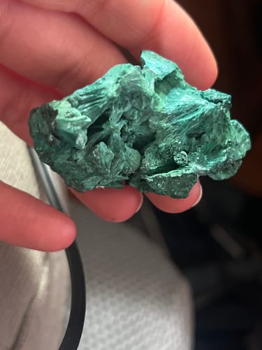 Customer's hand holding a rough, green Natural Phoenix Raw Stone from the VIP Crystal Club.