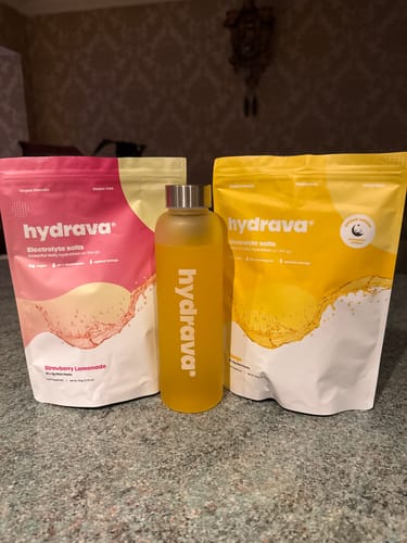 Reviewer's pouches of Strawberry Lemonade and Mango hydrava electrolyte salts with a branded bottle filled with the drink.