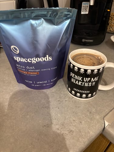 Customer's bag of Astro Dust on a counter, next to a mug with the prepared, frothy chocolate drink.