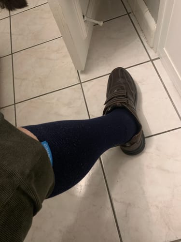 Reviewer's leg wearing a dark blue Performance Eucalyptus Compression Sock with a brown shoe on a tiled floor.