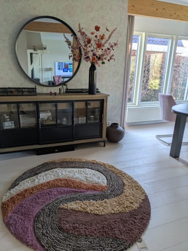 Klant toont het ronde, veelkleurige HKliving Tufted vloerkleed op een lichte vloer.