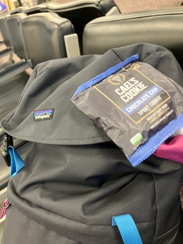 Reviewer's individually packaged Cael's Cookie on a backpack in a travel waiting area.