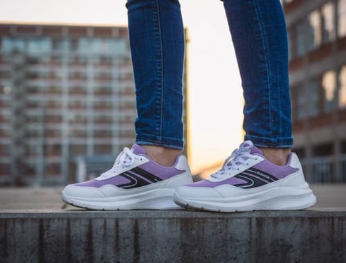 Customer wearing the purple and white Easy Fit shoes with jeans while standing on a concrete ledge.