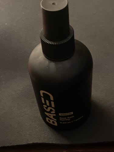 Customer's matte black bottle of Based Sea Salt Spray on a dark surface.