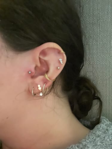 Close-up of a reviewer's ear showing the dangle flatback stud gold in the second lobe piercing among other earrings.