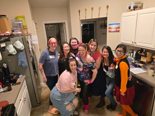 A group of customers in colorful 80s costumes posing for a photo while playing the Murder Mystery Game.