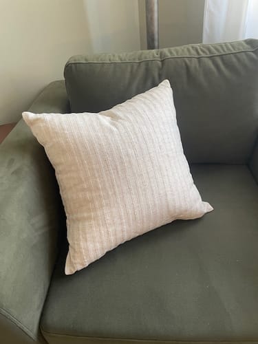 Customer's textured cream Mabel pillow cover resting on a green armchair.