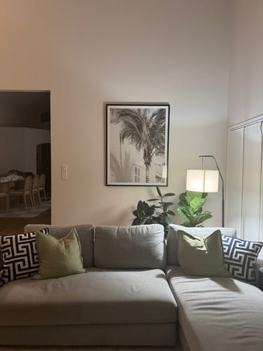 Customer's Hamptons Palm Art Print in a black frame hanging in a living room above a grey sectional sofa.