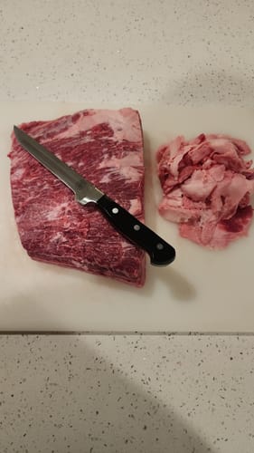 Customer trimming a marbled USDA Choice Bone-In Short Rib on a white cutting board with a knife.