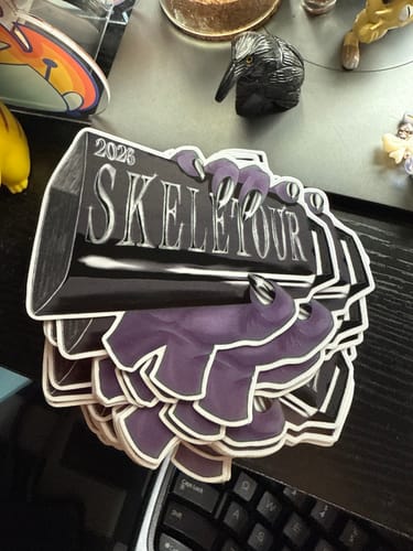 Customer's stack of custom vinyl stickers featuring a purple hand gripping a 'SKELETOUR' sign.