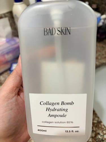 Reviewer holding the large, translucent bottle of Bad Skin Collagen Bomb Hydrating Ampoule.