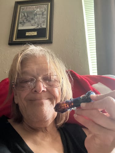A happy reviewer holding a blue glass pipe after enjoying the Cherry Dosi-Do strain.