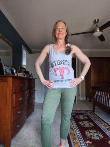 Reviewer smiling while wearing the light gray OBGYM Tank Top in a bedroom.